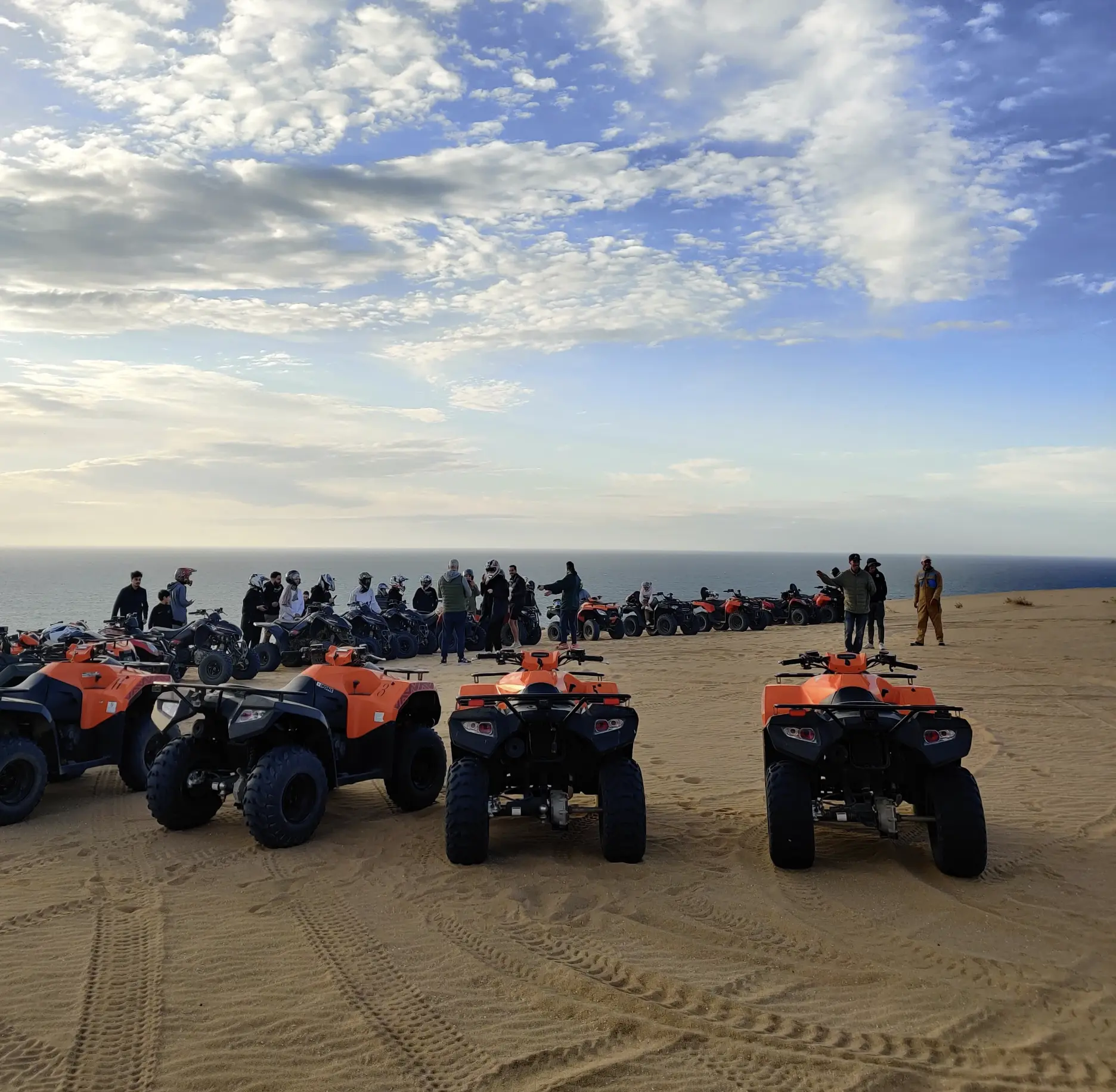 A group of people standing on a beach with their motorcycles.
