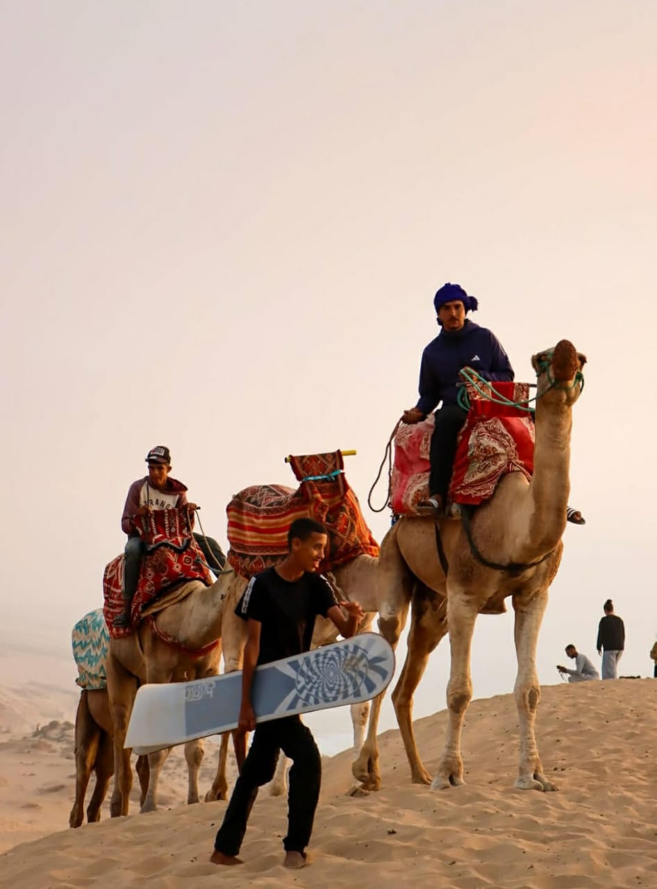 A man riding a camel with a surfboard.