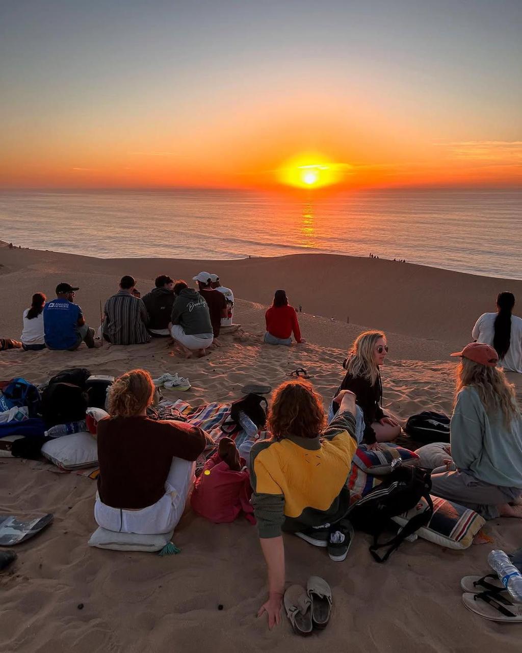 A group of people sitting on the beach watching the sunset.